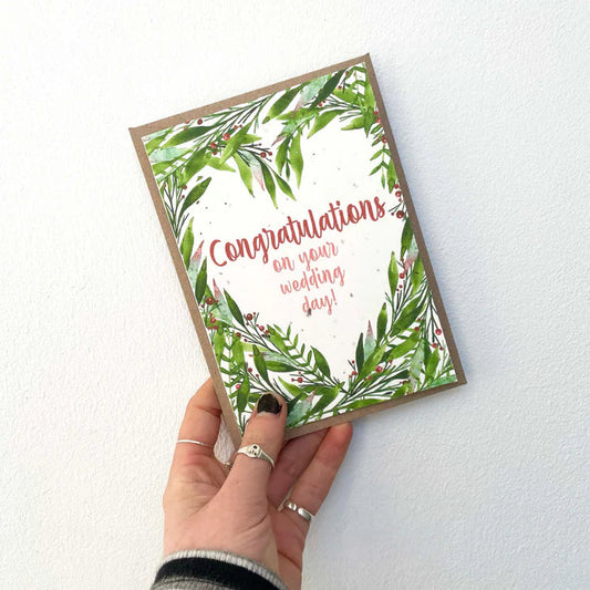 Hand holding a wedding congratulations card with greenery design on a white background