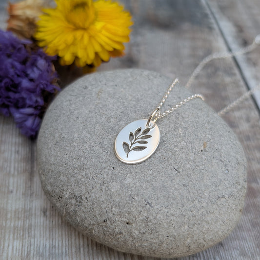 Silver necklace with a leaf pendant on a stone with flowers in the background