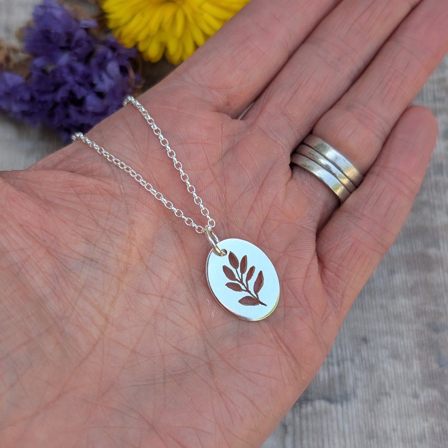 Silver necklace with a leaf pendant on a hand with flowers in the background
