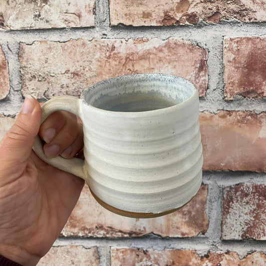 Hand holding a ceramic mug with a textured surface against a brick wall.