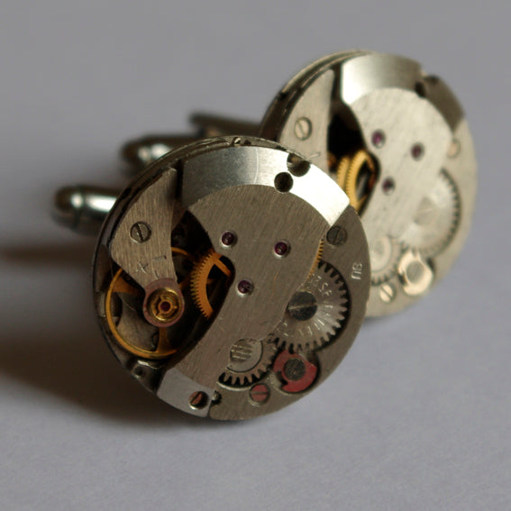 A pair of silver-coloured cufflinks featuring intricate vintage watch mechanisms as their design.